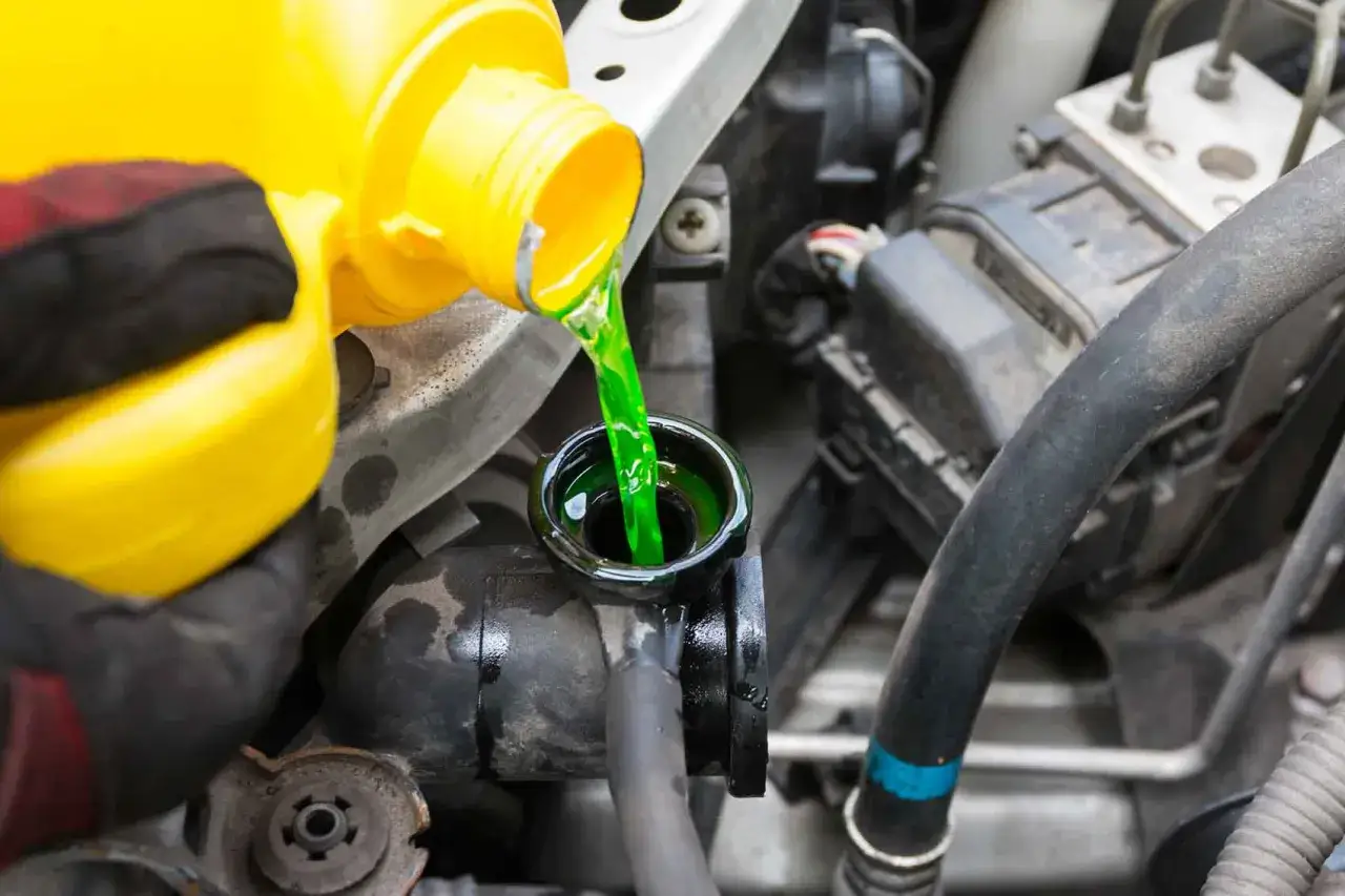 Main verte, un liquide de refroidissement, est versée d'une bouteille jaune dans le réservoir d'un moteur de voiture.