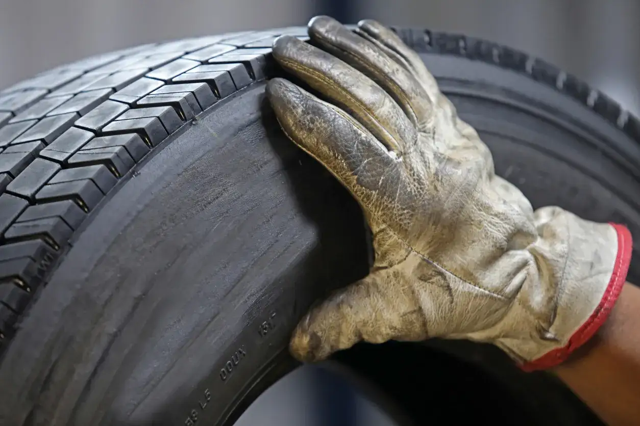 Main d'un mécanicien en gant vérifiant l'usure d'un pneu, étape clé pour savoir comment acheter une voiture d'occasion en toute sécurité.