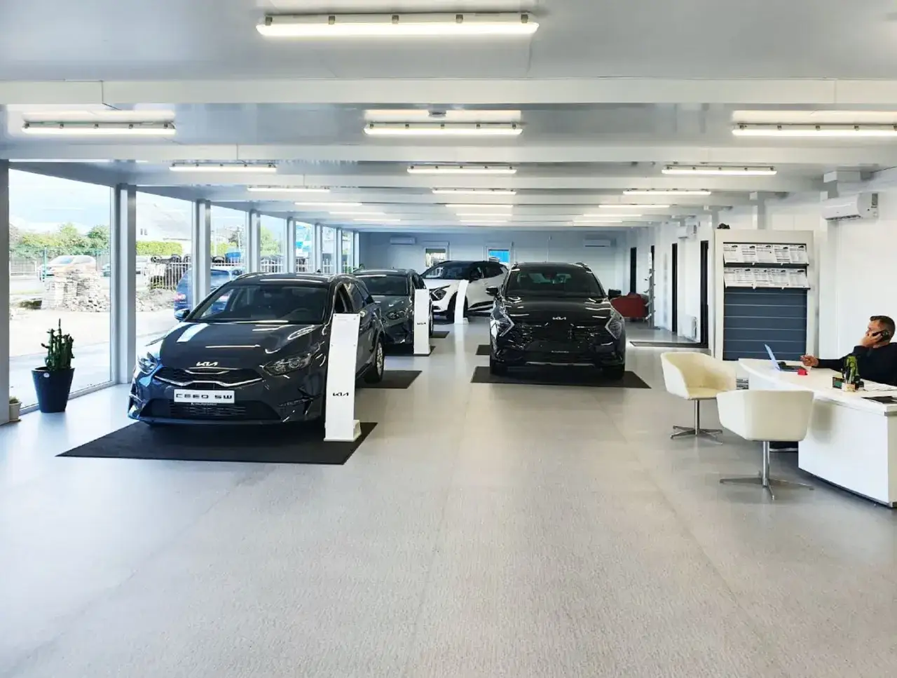 Intérieur d'un concessionnaire automobile moderne, avec plusieurs voitures neuves alignées. Un homme est au téléphone à son bureau, prêt à gérer votre dépôt vente véhicule.