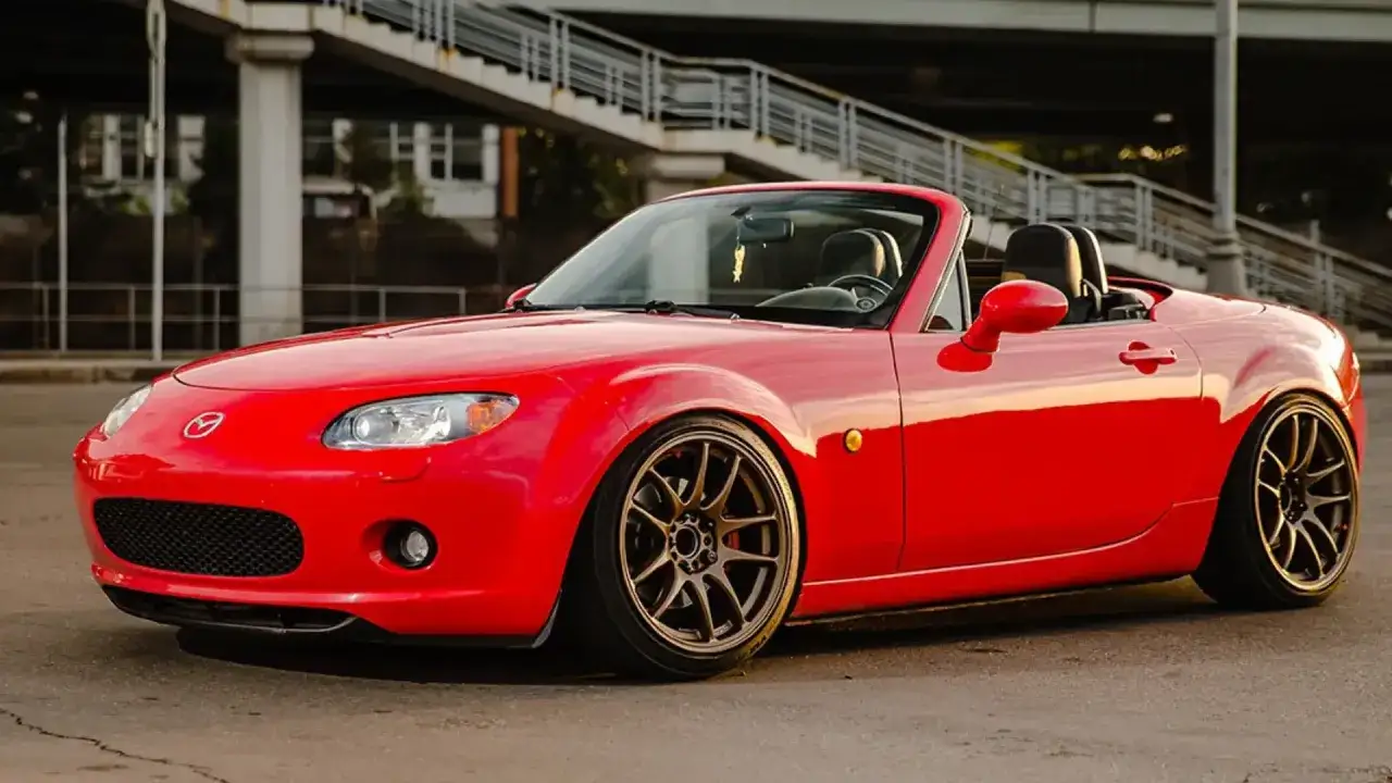 Mazda MX-5 rouge rabaissée, jantes bronze. La voiture sport idéale pour un jeune permis rêvant de liberté.