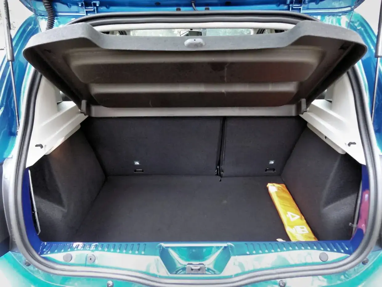 Le coffre d'une Dacia Sandero, vide et prêt à accueillir vos bagages. Un triangle de signalisation jaune est visible sur le côté.