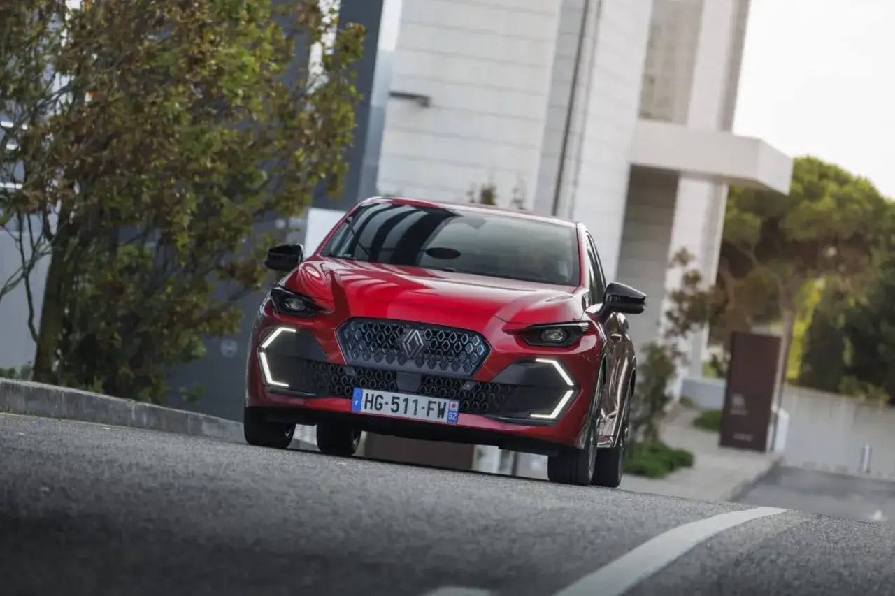 Une petite voiture confortable pour faire de la route, rouge vif, roule sur une route asphaltée devant un bâtiment moderne.