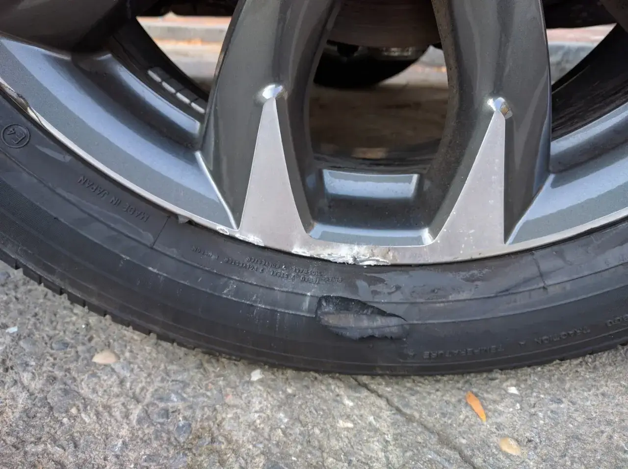 Gros plan sur un pneu abîmé sur le flanc, probablement suite à un choc contre le trottoir. La jante grise présente des éraflures.