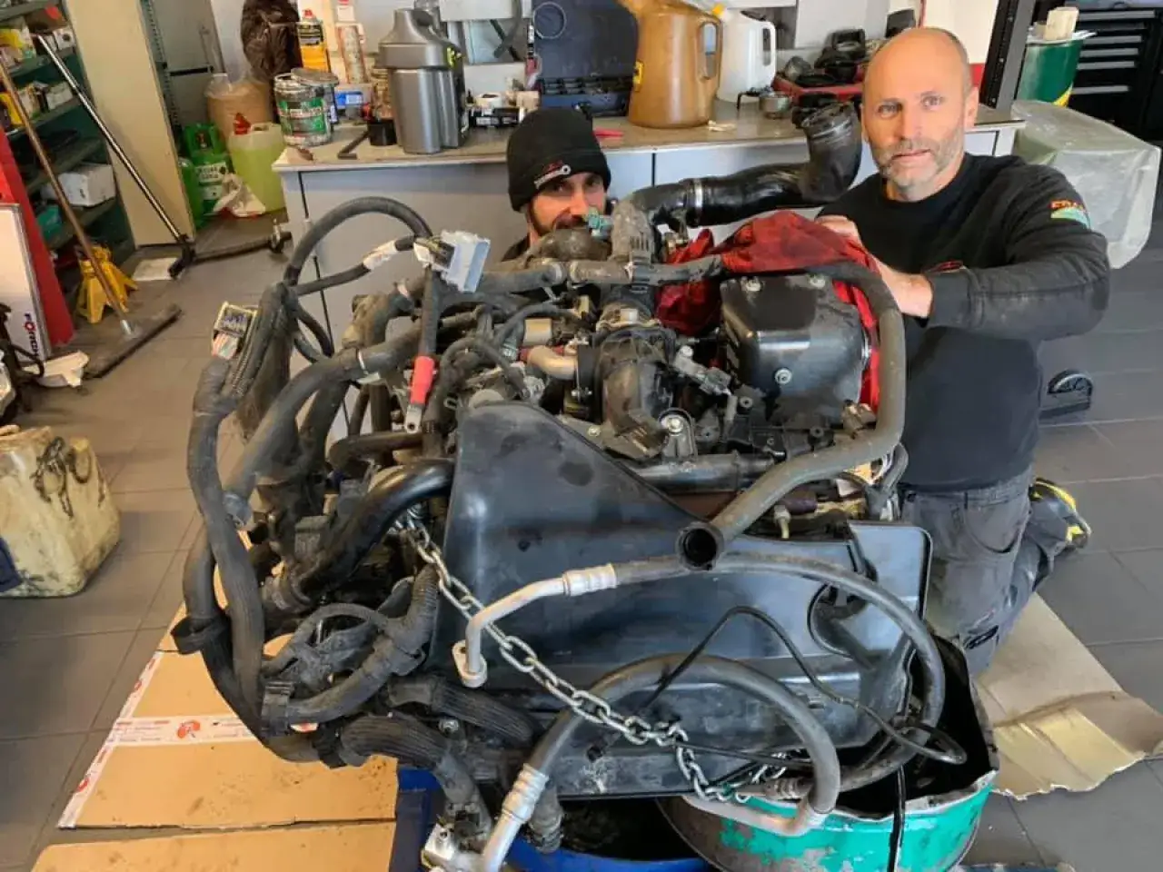 Deux mécaniciens travaillent sur un moteur pour un échange standard. L'un est penché sur le moteur, l'autre le regarde.