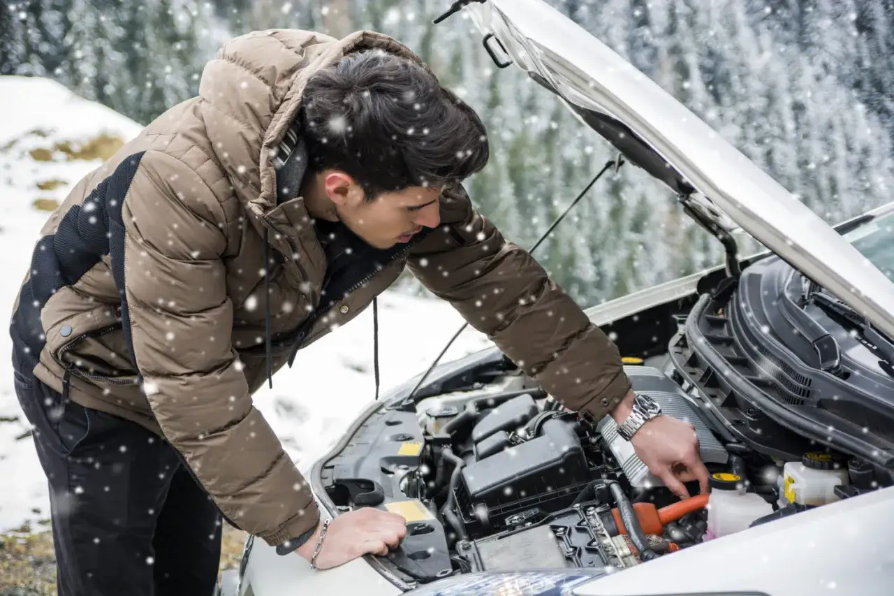 Un homme en doudoune vérifie le moteur de sa voiture sous la neige. Une astuce pour démarrage à froid diesel peut être utile par ce temps.