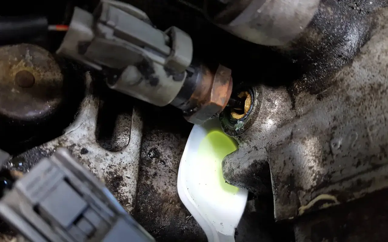 Une fuite de liquide de refroidissement couleur verte s'échappe d'un composant moteur, visible sur un plateau blanc.