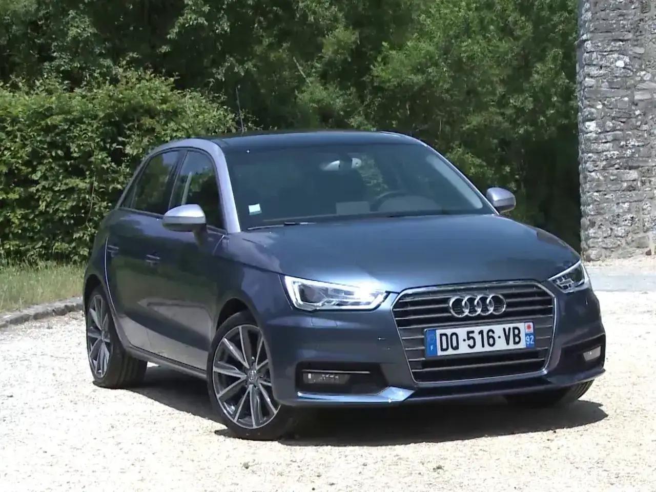 Audi A1 1.0 TFSI 95, une voiture compacte réputée pour sa fiabilité, garée devant un mur de pierre et des arbres.