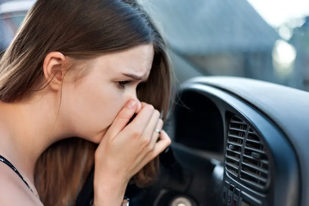 Une femme se pince le nez, visiblement incommodée par l'odeur climatisation voiture.