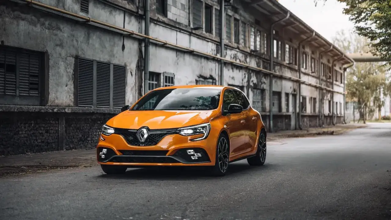 Une Renault Mégane R.S. orange vif, garée devant un bâtiment industriel délabré. Un excellent choix pour le prix moyen d'une voiture d'occasion sportive.