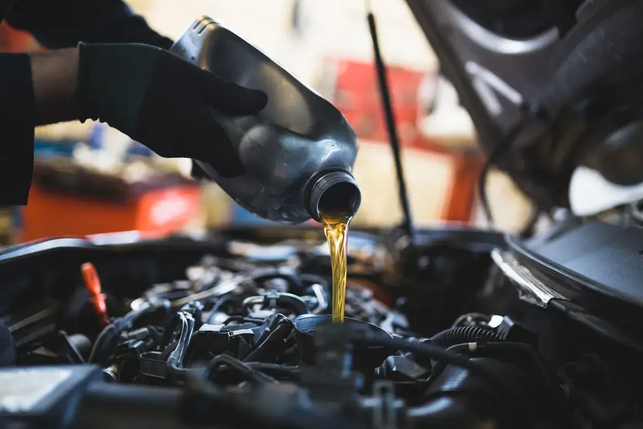 Main d'un mécanicien versant du liquide de transmission dans le moteur d'une voiture.