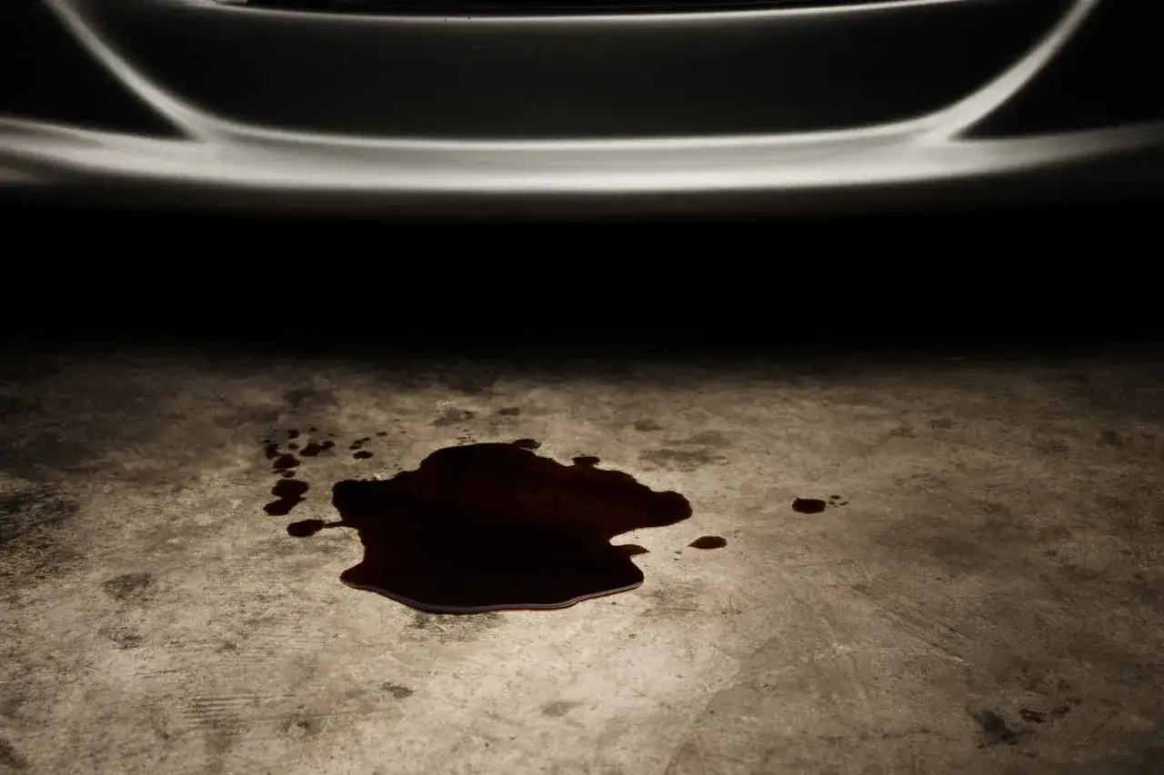 Tache d'huile sur le sol, signe d'une fuite d'huile carter moteur. La voiture est garée, le problème est visible.
