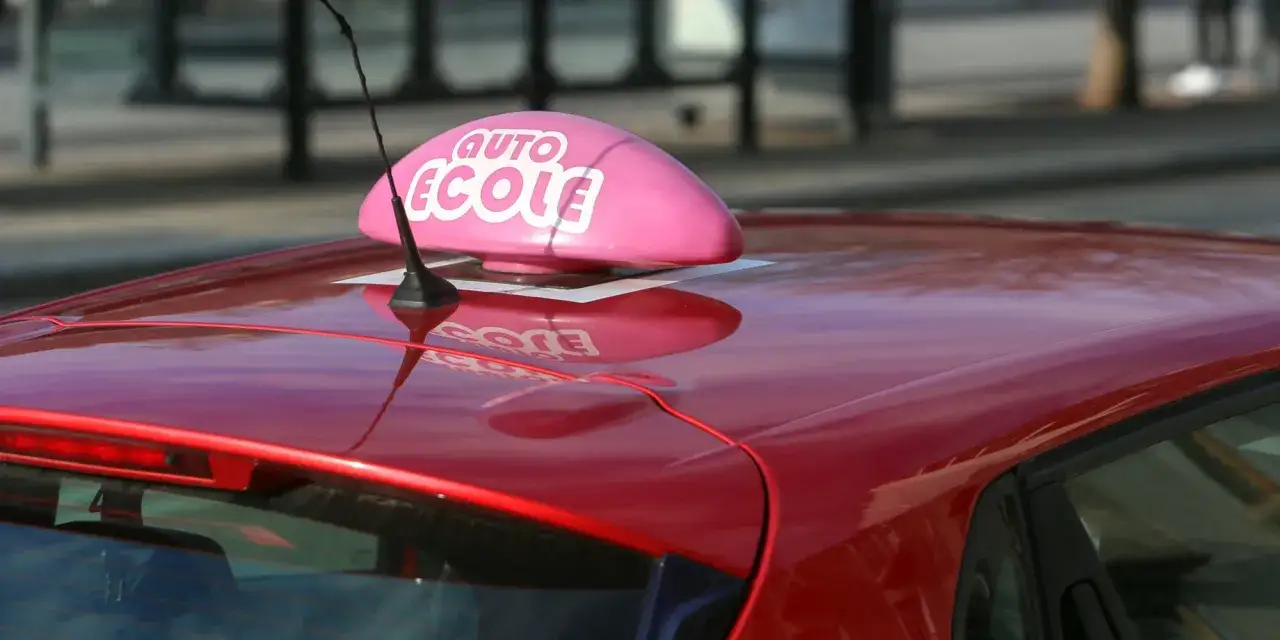 Voiture rouge d'auto-école avec un panneau rose. L'image évoque le permis à 17 ans, une étape vers la responsabilité.