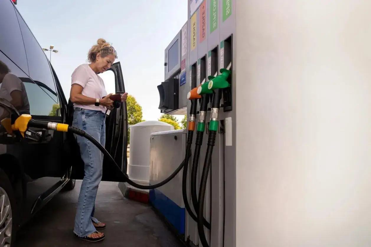Femme à la station-service, vérifiant sa carte grise pour choisir entre essence ou diesel. Le pistolet de la pompe est prêt.