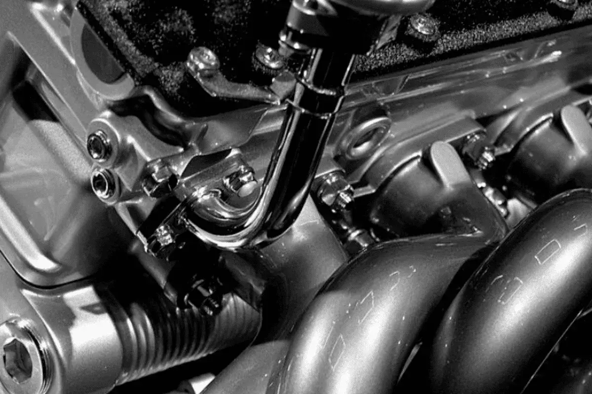 Gros plan sur un moteur de voiture essence, avec des tuyaux chromés et des boulons. On dirait que la voiture qui broute en roulant essence a un problème mécanique.