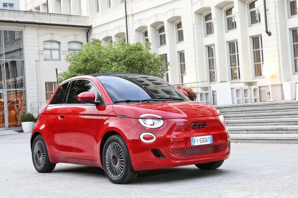 Fiat 500 rouge garée devant un bâtiment blanc. Le pression des pneus est parfaite pour une conduite urbaine.