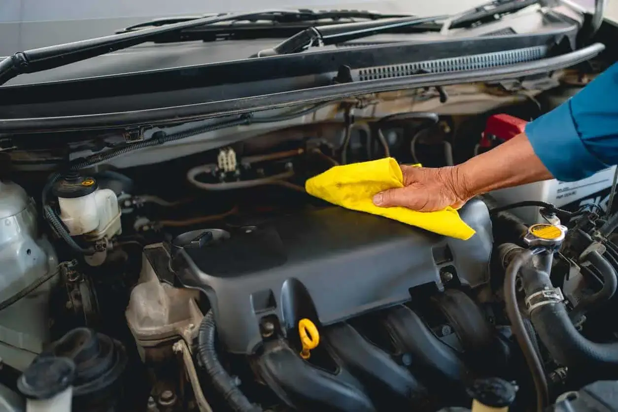 Main d'un mécanicien utilisant un chiffon jaune pour nettoyer l'huile moteur d'une voiture.