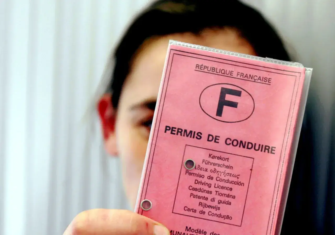 Une personne tient un permis de conduire français rose. L'âge de 17 ans est souvent l'âge minimum pour obtenir ce permis.