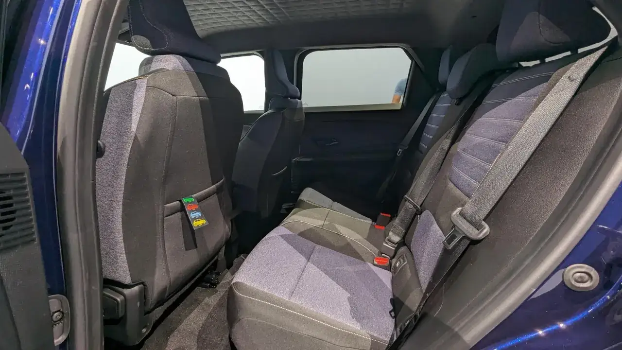 Intérieur d'une voiture bleue, sièges arrière en tissu gris et bleu, avec une étiquette décorative de petites voitures. L'espace suggère le confort d'une dimension R5 électrique.