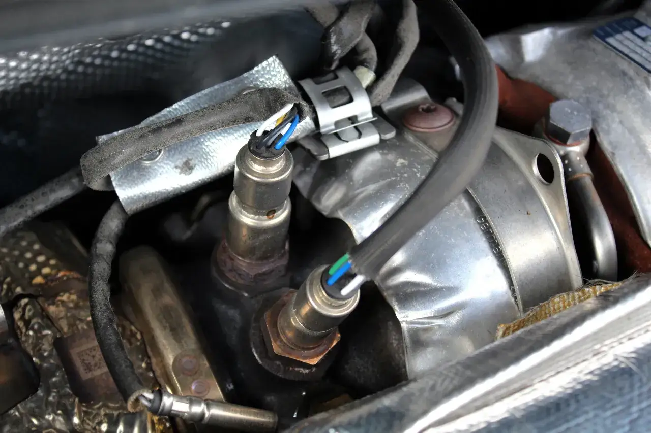 Détail de deux sondes lambda avec leurs câbles colorés, prêtes pour une reprogrammation. L'une est vissée sur un collecteur moteur.