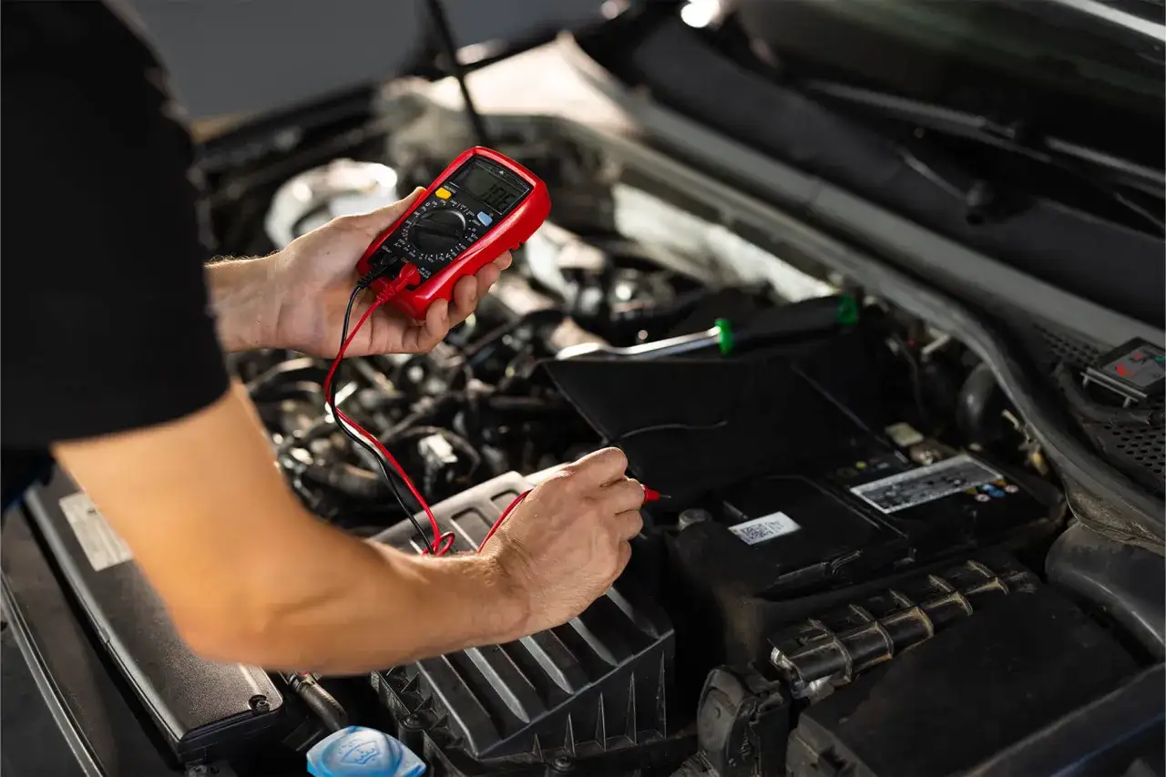Un mécanicien vérifie la batterie d'une voiture qui cale en roulant avec un multimètre rouge.