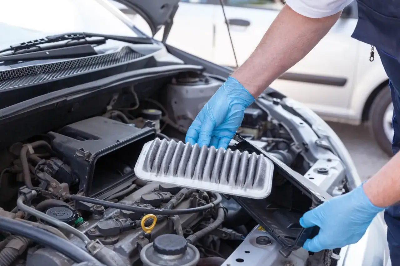 Main tenant, mains gantées, procède au changement du filtre à air encrassé de la voiture.