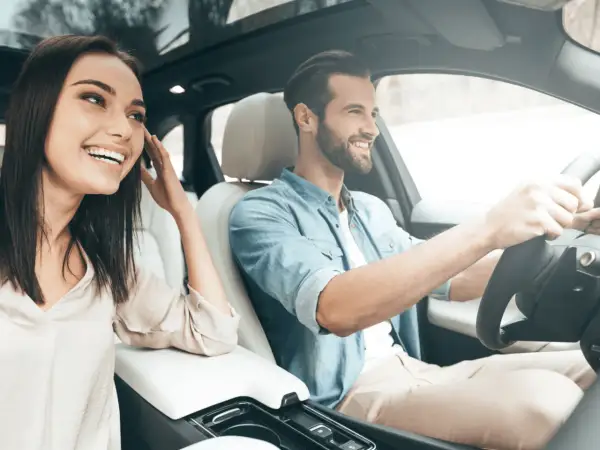 Un jeune homme souriant conduit, sa compagne à ses côtés, profitant de la **conduite supervisée accompagnateur**.