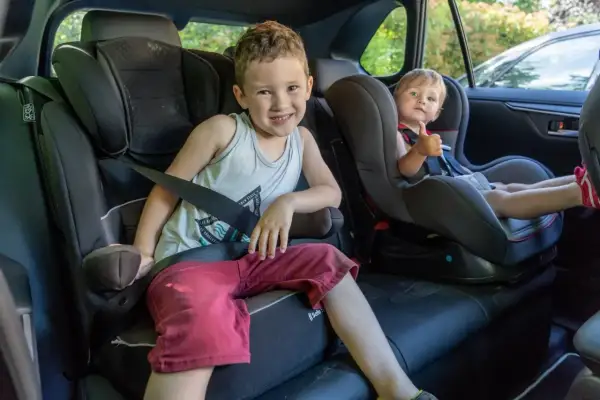 Deux enfants souriants dans leurs sièges auto, prêts pour le transport en voiture. Le plus grand fait un clin d'œil, le plus jeune montre son pouce levé.