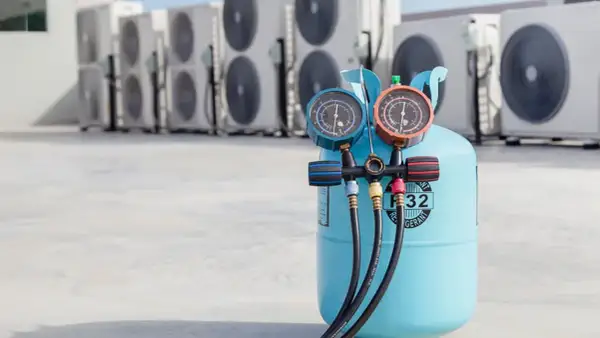 Bouteille de gaz R32 pour climatisation de voiture, avec manomètres, devant des unités extérieures de climatisation.