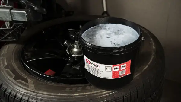 Un seau de pâte pour monter les pneus, vis dans pneu, est posé sur un pneu noir.