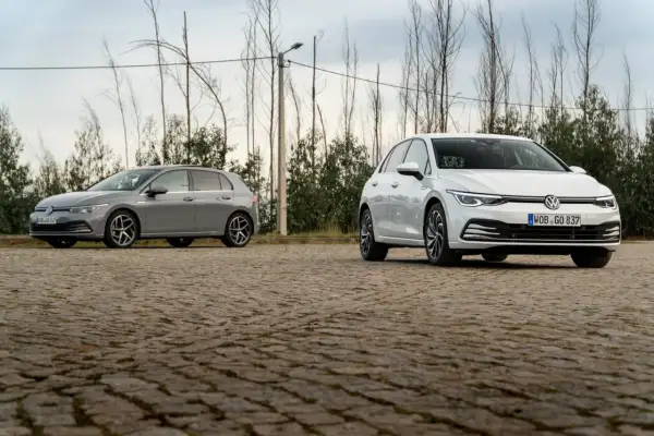 Deux Volkswagen Golf 8, une grise et une blanche, stationnées sur un sol pavé. La longueur de la Golf 8 est bien mise en valeur.