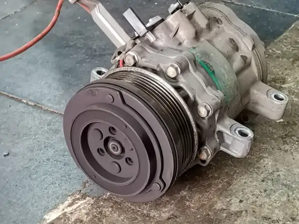 Compresseur de climatisation automobile, prêt pour son remplacement. Pièce mécanique essentielle pour le confort de conduite.
