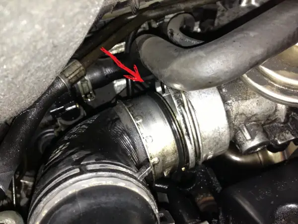 Flèche rouge pointe une durite turbo percée, suintant de l'huile dans le compartiment moteur.