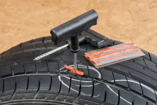 Kit de réparation pour pneu de voiture : un outil insère une mèche dans un pneu crevé, prêt à réparer.