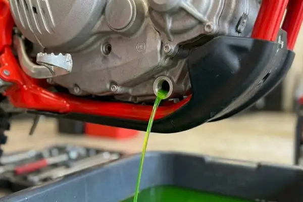 Vidange du liquide de refroidissement OAT d'une moto. Le liquide vert vif s'écoule du moteur dans un bac de récupération.