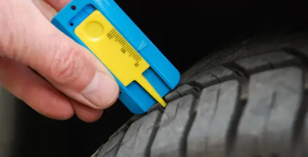 Mesure de la bande de roulement d'un pneu avec un jauge. Le résultat indique une usure trop importante, synonyme de refus contrôle technique pneu.