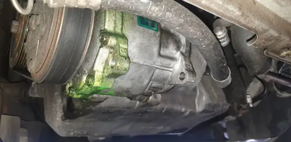 Recherche fuite clim auto : le compresseur est couvert d'un liquide vert fluorescent, signe d'une fuite.