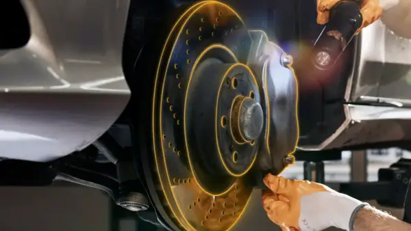 Inspection d'un frein de service de voiture. Un mécanicien utilise une lampe torche pour examiner le disque et l'étrier.